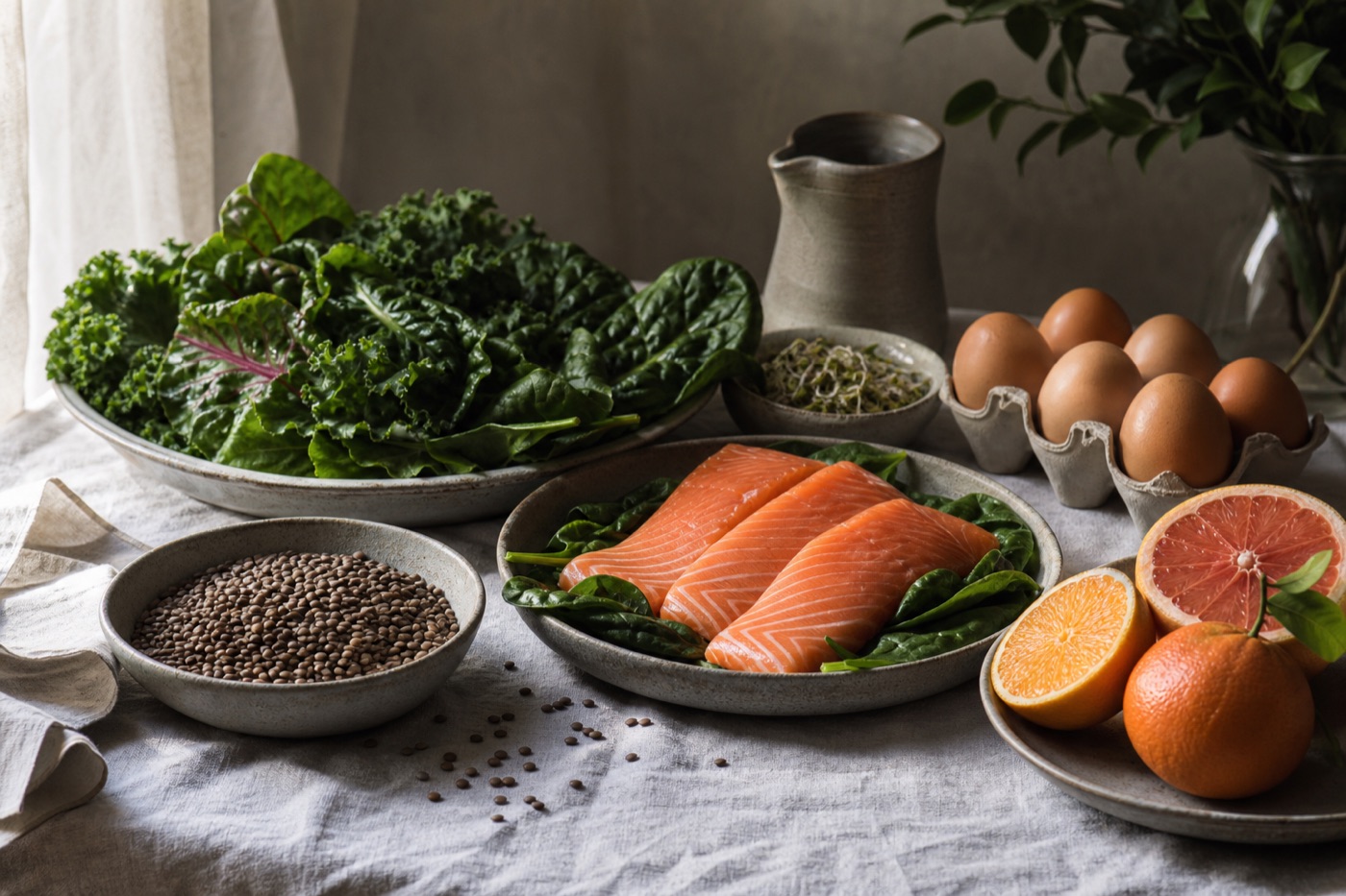 Editorial still life of leafy greens, lentils, salmon, eggs and citrus on a linen cloth
